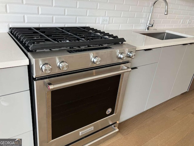 details with stainless steel range with gas cooktop, white cabinets, sink, tasteful backsplash, and light hardwood / wood-style floors