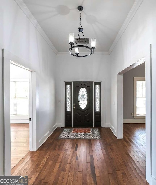 foyer entrance with ornamental molding, an inviting chandelier, and dark hardwood / wood-style floors