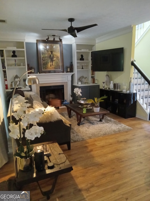 living room featuring a fireplace, a ceiling fan, stairway, light wood-type flooring, and crown molding