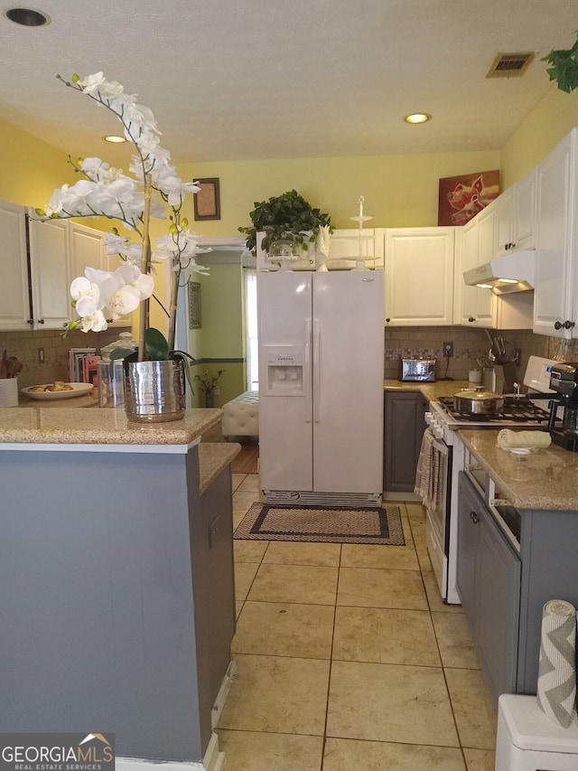 kitchen featuring under cabinet range hood, white appliances, visible vents, white cabinets, and backsplash