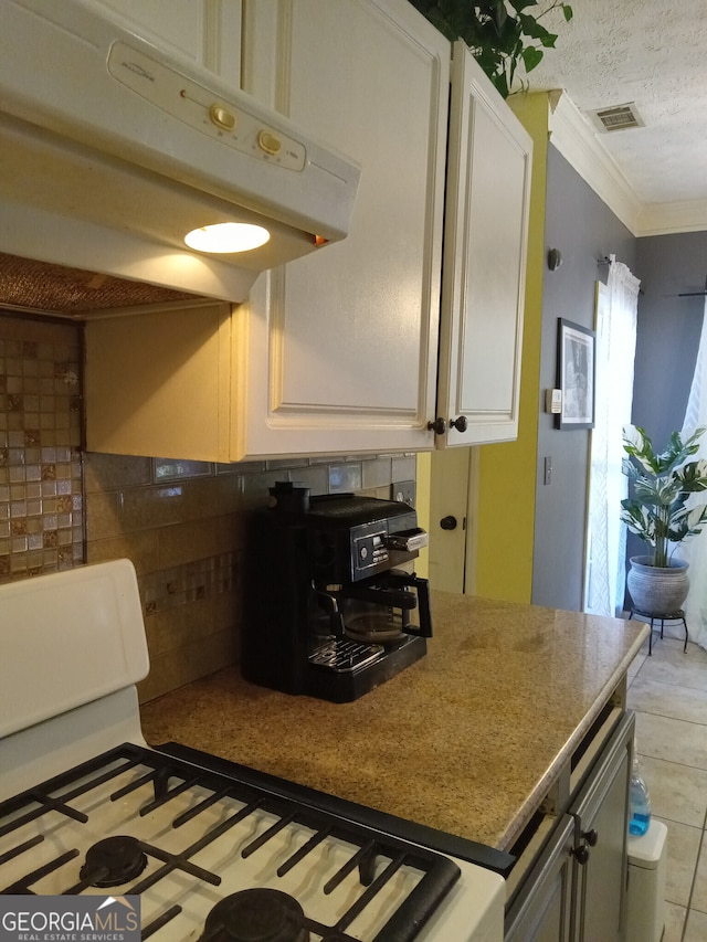 kitchen featuring under cabinet range hood, gas range oven, white cabinetry, and ornamental molding