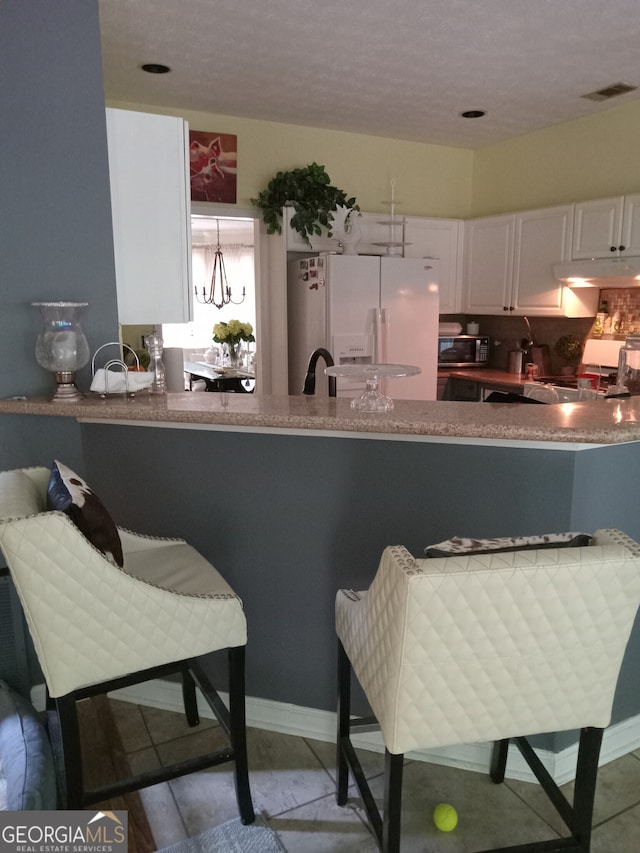 kitchen with a peninsula, white refrigerator with ice dispenser, white cabinetry, hanging light fixtures, and range