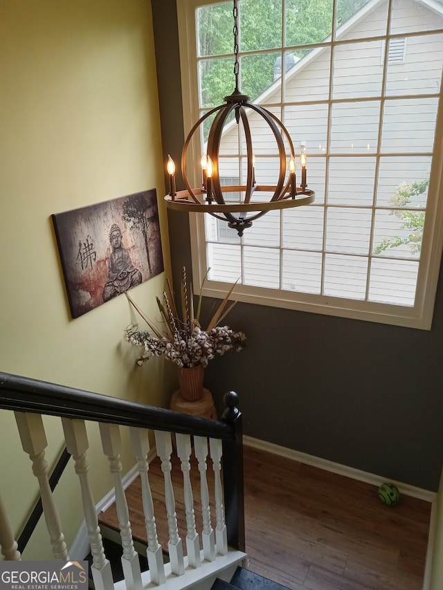 stairs with a wealth of natural light, an inviting chandelier, baseboards, and wood finished floors