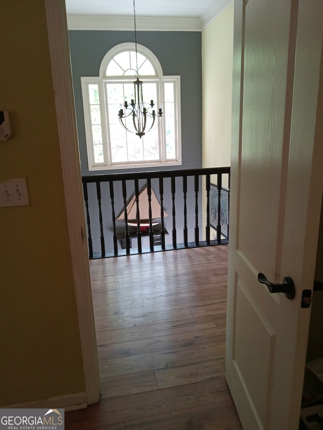 corridor featuring wood finished floors, crown molding, and an inviting chandelier