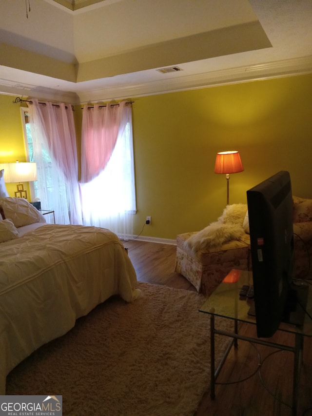 bedroom featuring a tray ceiling, crown molding, visible vents, wood finished floors, and baseboards