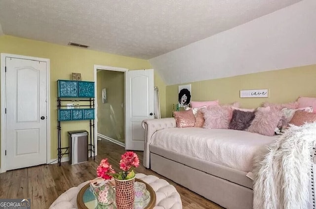 bedroom with lofted ceiling, a textured ceiling, visible vents, and wood finished floors