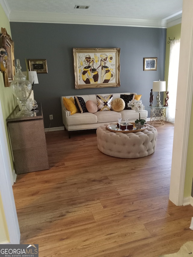 living room featuring ornamental molding, light wood finished floors, visible vents, and baseboards