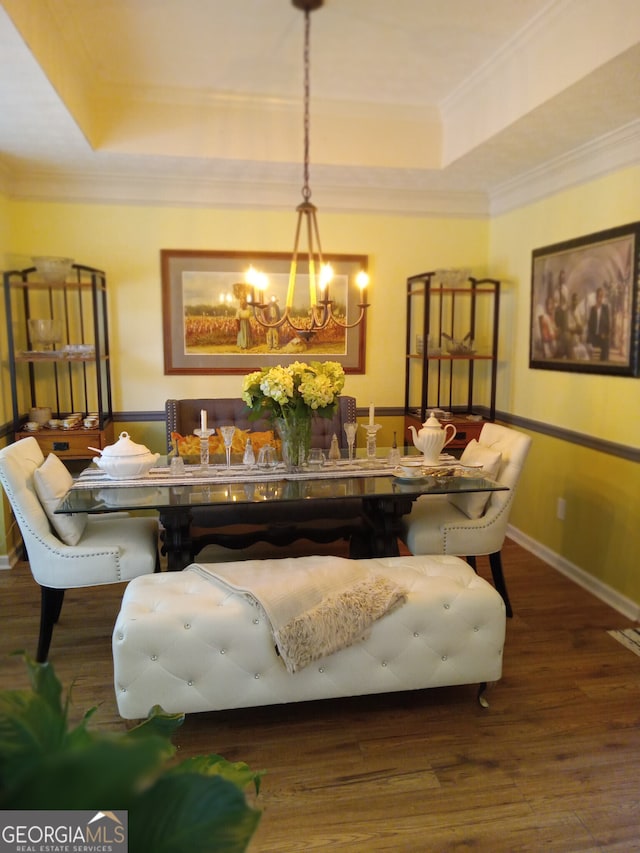 dining space featuring dark wood-type flooring, a raised ceiling, a chandelier, and ornamental molding