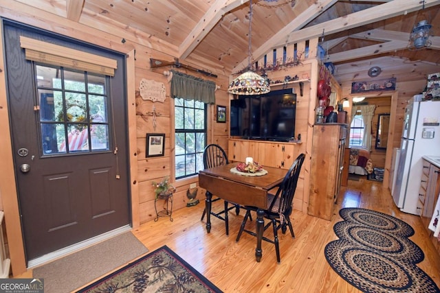 dining room featuring vaulted ceiling with beams, light hardwood / wood-style flooring, wood walls, and wooden ceiling