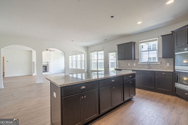 kitchen featuring light wood-type flooring, a kitchen island, backsplash, sink, and light stone counters