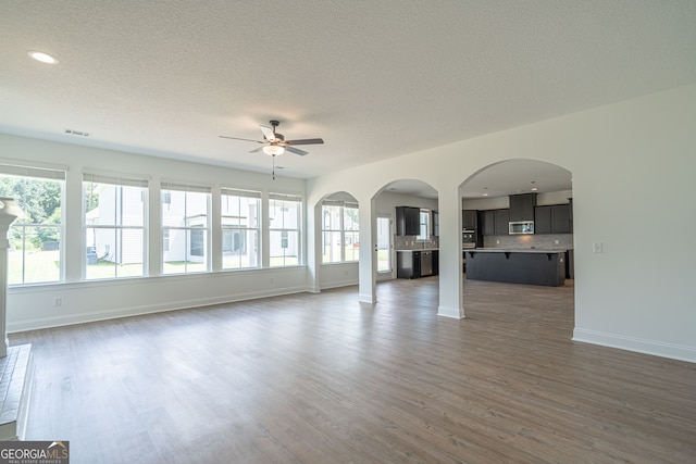 unfurnished living room featuring a textured ceiling, dark hardwood / wood-style flooring, and ceiling fan