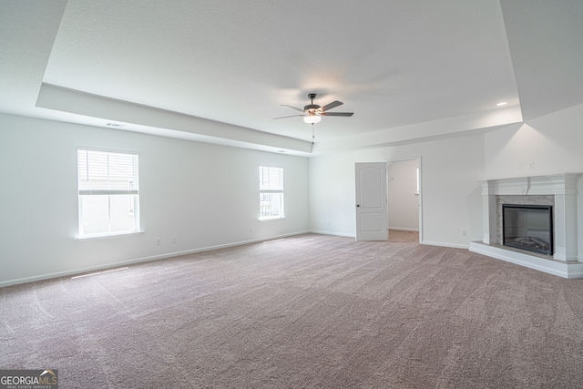 unfurnished living room featuring carpet flooring, a high end fireplace, ceiling fan, and a raised ceiling