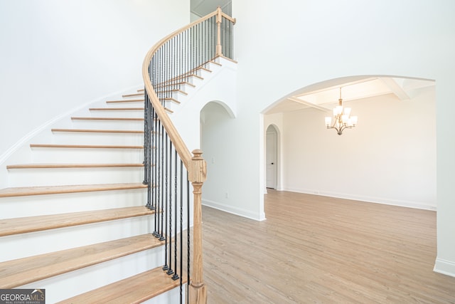 stairs featuring wood-type flooring, an inviting chandelier, and a towering ceiling