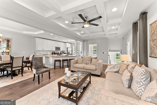 living room featuring ceiling fan, coffered ceiling, light wood-type flooring, and beam ceiling