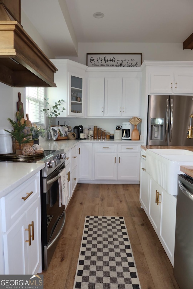 kitchen with custom exhaust hood, white cabinetry, appliances with stainless steel finishes, and hardwood / wood-style floors