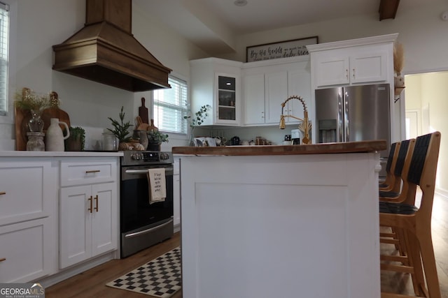 kitchen featuring premium range hood, stainless steel refrigerator with ice dispenser, white cabinets, light hardwood / wood-style floors, and range with electric stovetop