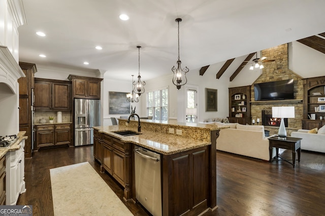 kitchen featuring appliances with stainless steel finishes, dark wood-type flooring, a center island with sink, and a fireplace