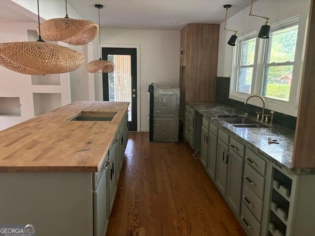 kitchen featuring dark wood-type flooring, hanging light fixtures, black electric stovetop, sink, and butcher block counters