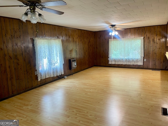 spare room with heating unit, ceiling fan, wooden walls, and light hardwood / wood-style flooring