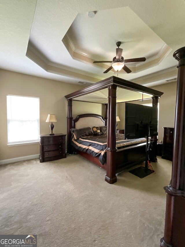 carpeted bedroom with ceiling fan, a raised ceiling, and ornate columns