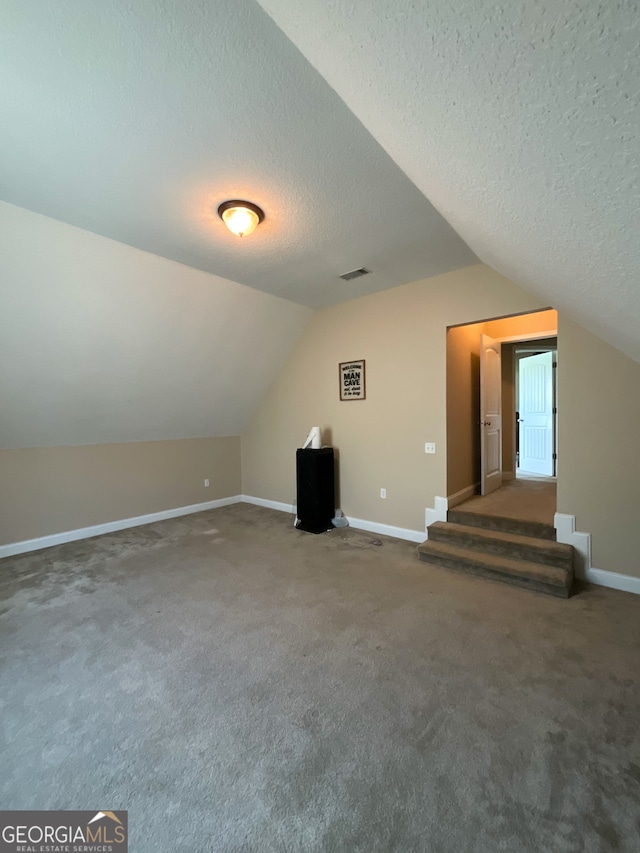 additional living space featuring carpet, vaulted ceiling, and a textured ceiling