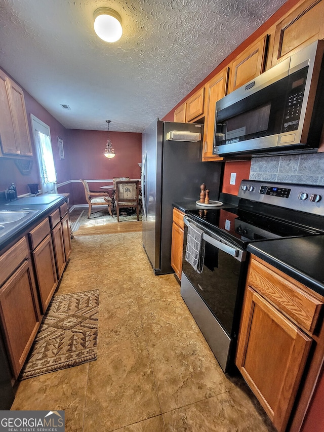 kitchen featuring decorative backsplash, a textured ceiling, appliances with stainless steel finishes, hanging light fixtures, and light tile patterned floors