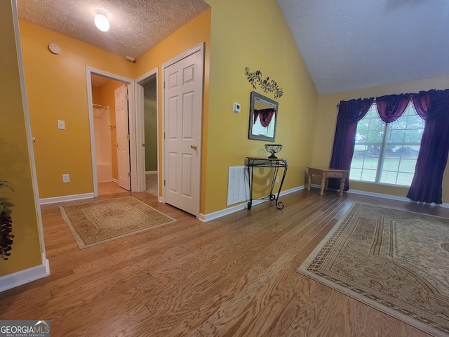 foyer featuring wood-type flooring, vaulted ceiling, and a textured ceiling