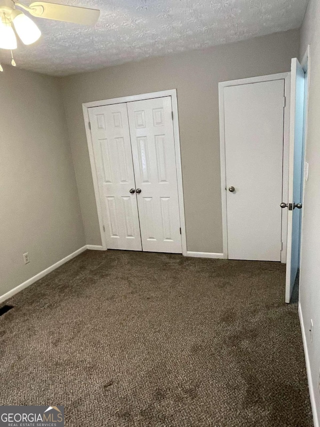 unfurnished bedroom with dark colored carpet, ceiling fan, a textured ceiling, and a closet