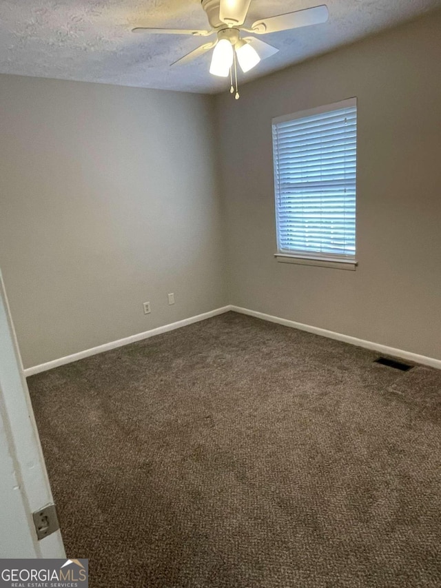 spare room with ceiling fan, dark carpet, and a textured ceiling