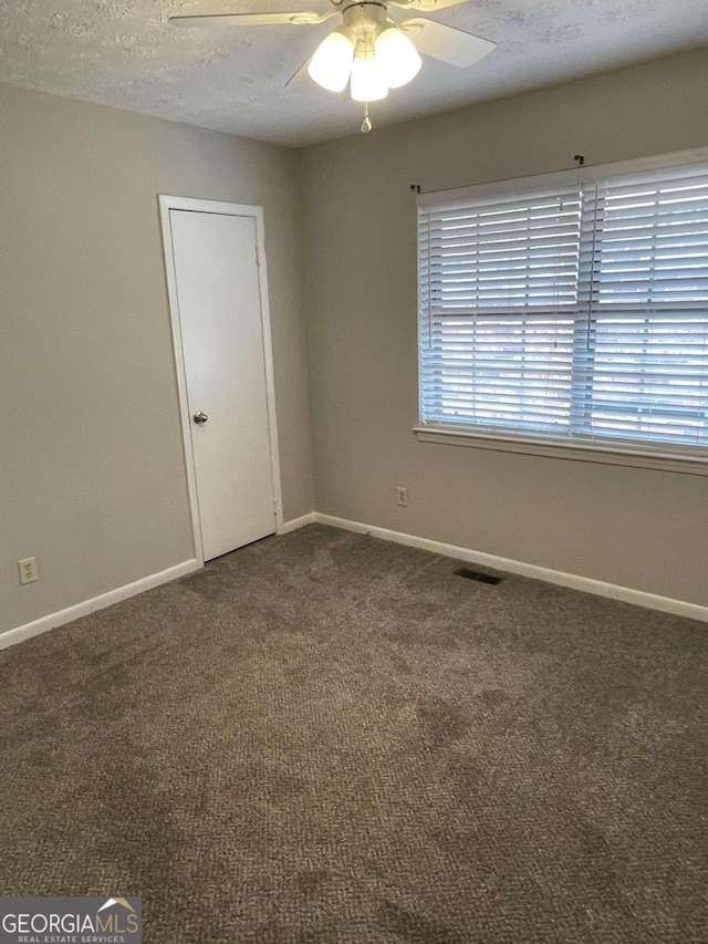 empty room with ceiling fan, a textured ceiling, and dark colored carpet