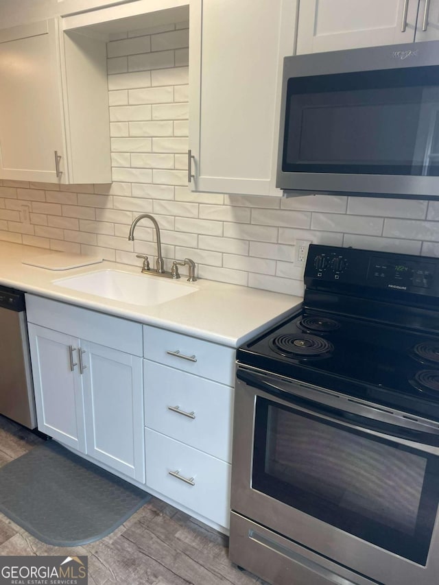 kitchen with sink, tasteful backsplash, stainless steel appliances, hardwood / wood-style floors, and white cabinets