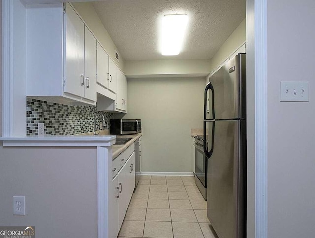 kitchen featuring backsplash, a textured ceiling, stainless steel appliances, light tile patterned floors, and white cabinets