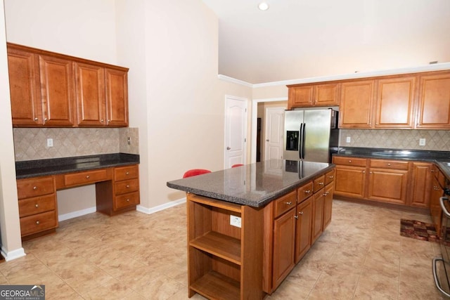 kitchen with a center island, tasteful backsplash, built in desk, ornamental molding, and stainless steel fridge with ice dispenser