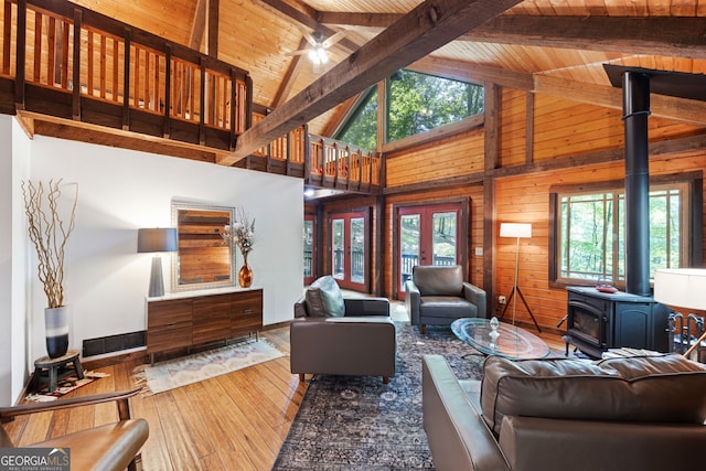 living room with a wood stove, high vaulted ceiling, wooden walls, ceiling fan, and wooden ceiling