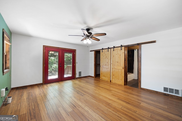 interior space with ceiling fan, a barn door, wood-type flooring, and french doors