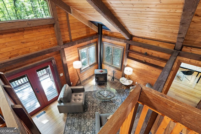 living room with vaulted ceiling with beams, a wood stove, wooden walls, wooden ceiling, and hardwood / wood-style flooring