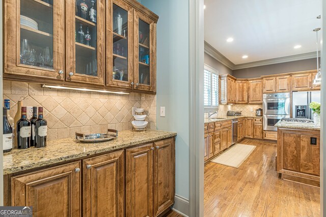 kitchen featuring crown molding, tasteful backsplash, light hardwood / wood-style flooring, stainless steel appliances, and light stone countertops