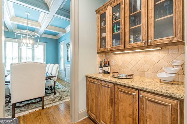 kitchen featuring coffered ceiling, tasteful backsplash, a chandelier, hanging light fixtures, and hardwood / wood-style flooring