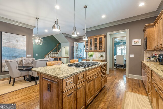 kitchen with a kitchen island, pendant lighting, appliances with stainless steel finishes, light hardwood / wood-style floors, and ornamental molding