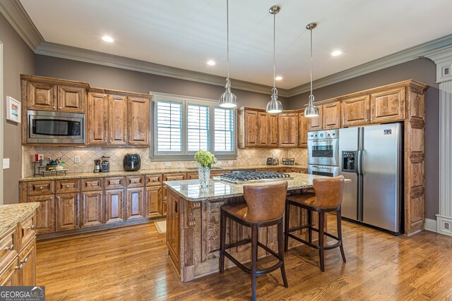 kitchen with light wood-type flooring, appliances with stainless steel finishes, a center island, and light stone countertops