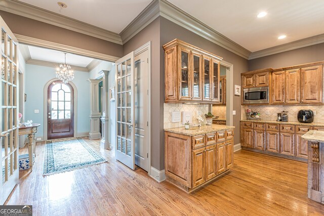 foyer featuring light wood-type flooring, an inviting chandelier, crown molding, and ornate columns