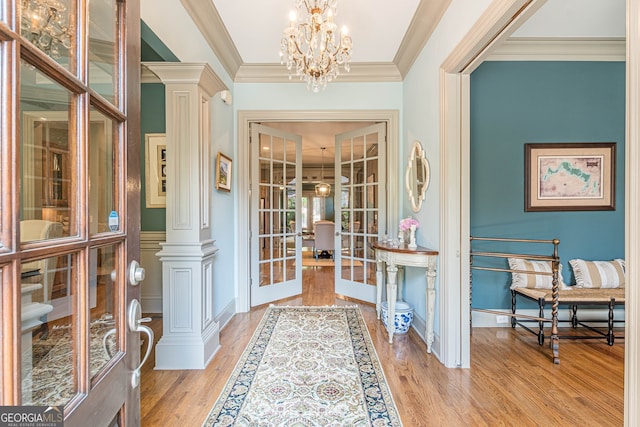 foyer entrance featuring light hardwood / wood-style flooring, french doors, decorative columns, crown molding, and a chandelier