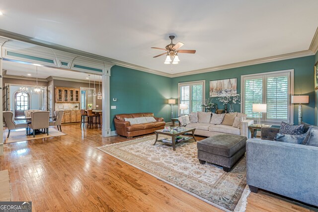 living room featuring ceiling fan with notable chandelier, ornamental molding, light hardwood / wood-style floors, and a healthy amount of sunlight