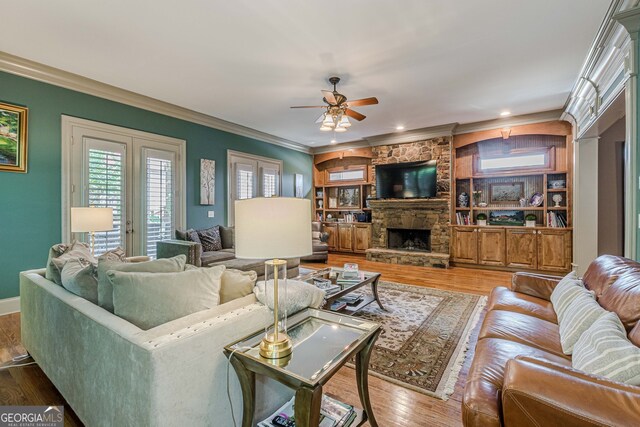 living room with a fireplace, hardwood / wood-style floors, built in features, ornamental molding, and ceiling fan