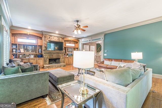 living room featuring hardwood / wood-style floors, built in shelves, a stone fireplace, ceiling fan, and ornamental molding