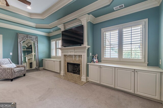 carpeted living room with a high end fireplace, a raised ceiling, crown molding, and ceiling fan