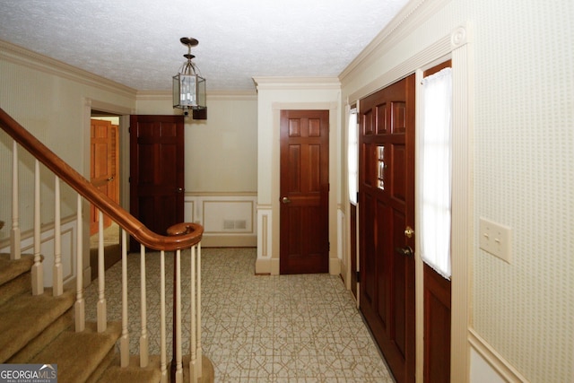 hall featuring a wainscoted wall, stairway, ornamental molding, a textured ceiling, and wallpapered walls