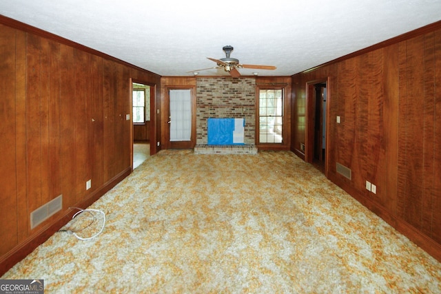 unfurnished living room featuring carpet floors, visible vents, a fireplace, and wood walls