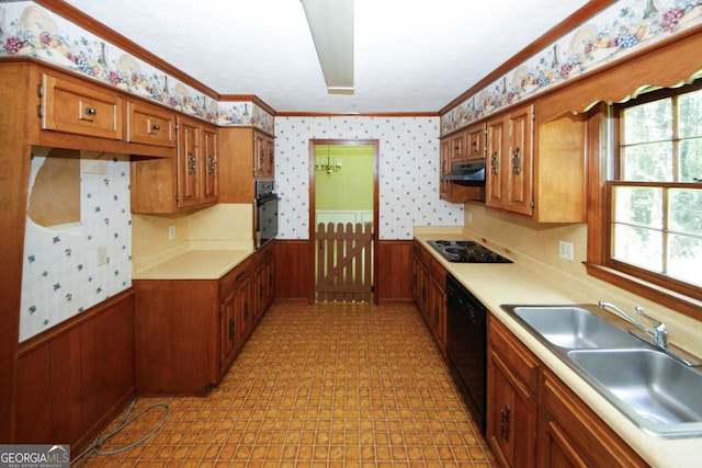 kitchen with wallpapered walls, a wainscoted wall, light countertops, black appliances, and a sink