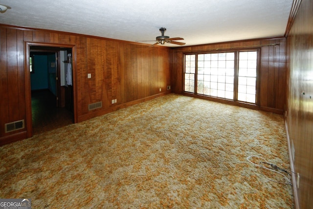 carpeted spare room featuring visible vents, crown molding, wooden walls, and ceiling fan